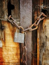 A weathered wooden door displays a rusty padlock and heavy chain, emphasizing neglect and