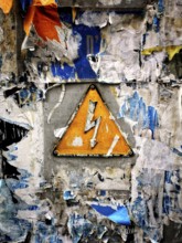 A bright yellow warning sign featuring a lightning bolt is mounted on a wall heavily covered with