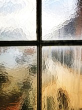 A textured glass window shows raindrops trickling down. The blurred outlines of an urban landscape