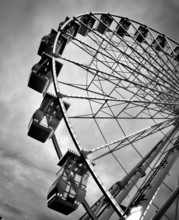 A large Ferris wheel stands prominently against a backdrop of clouds, its illuminated cabins