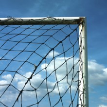 A football goal net is positioned against a cloudy sky, showcasing the intricate details of the