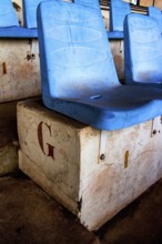 Rows of empty blue seats rest on a weathered concrete base in a deserted sports arena, highlighting