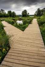 A wooden path stretches through fertile countryside in Auvergne, France, inviting exploration amid