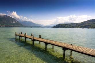 Clear skies reflect on the calm waters of Annecy lake, while a wooden pontoon invites visitors to