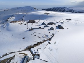 Spacious huts in snow-covered mountains with masts under a clear sky, aerial view, Aragaz, Aragac,