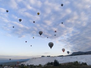 Hot air balloons float over a picturesque landscape under a cloudy sky, aerial view, Pamukkale,