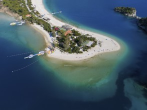 Aerial view of a narrow island with a sandy beach, surrounded by turquoise blue sea and wooded