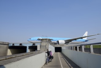 Aeroplane taxiing over a bridge over road and cycle path with cyclists, Amsterdam Airport Schiphol,