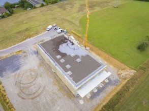 Aerial view of a building under construction with vehicles and crane on a wide field, green roof,