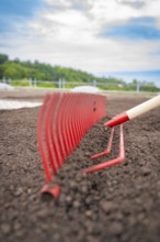 Close-up of a red rake working the soil on a roof, with nature in the background, roof greening,