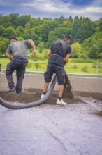 Two workers lay material with a hose on a roof on a green site, roof greening, house construction,