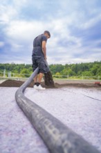 A construction worker distributes materials with a hose on a roof under a cloudy sky, roof