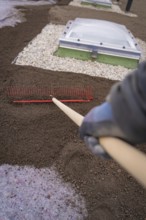A worker with a rake levels the ground on a roof with gravel beds, roof greening, house