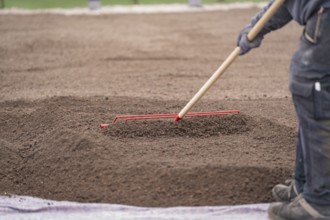 Person works the soil with a red rake, green roof, house construction, climate neutral