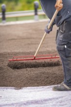 Man works the soil with a red rake, green roof, house construction, climate neutral