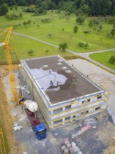 Building shell with crane and workers on a construction site surrounded by green areas, green roof,