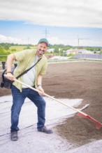 Man with rake smiling on a construction site on the roof of a building, roof greening, house