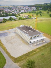 Aerial view of a rectangular building shell in a rural area near a housing estate, green roof,