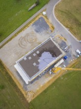 Aerial view of a rectangular building in shell construction on a large site next to a road, green