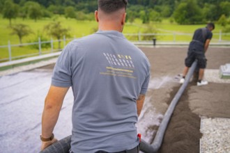 A worker in construction clothing holds a hose, with a view of a green landscape, roof greening,