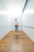 Woman standing in a modern lift with bright, minimalist design and wooden floor, Frieder Burda