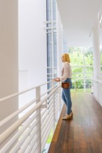A woman stands at a railing and looks through a large window at the surroundings, Frieder Burda