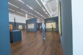 People looking at paintings in a modern art gallery with wooden floor and dark walls, Frieder Burda