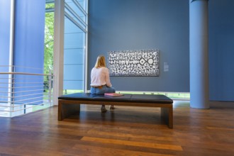 A woman sits on a bench in front of a modern work of art and looks at it attentively, Frieder Burda