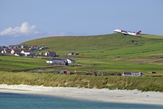 An aeroplane takes off over wide meadows and a coastal village with sea views, Sumburgh Head,