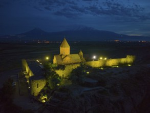 Illuminated monastery at night with mountains and shining stone walls, aerial view, Chor Wirap