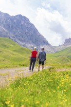 Couple hiking on a mountain path, surrounded by green meadows and mountains, Alpe di Siusi,