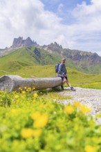 Man in the mountains sitting on a wooden bench, surrounded by green meadows and flowers, Alpe di