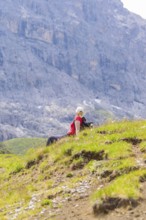 Person sitting on a green meadow, surrounded by rocky mountains under a blue sky, Alpe di Siusi,