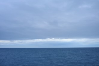 A calm sea stretches to the horizon with thick clouds in the sky, summer, Cook Strait, North