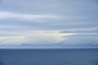 Calm sea under a dense canopy of clouds, mountains visible in the distance, summer, Cook Strait,