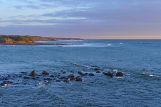Rocks in the sea under a pink-orange sky at sunset, summer, Opunake, Taranaki, North Island, New