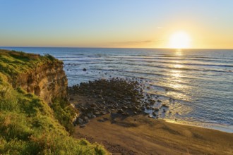 Sunset landscape with rocks and beach, warm colours dominate the scene, summer, Opunake, Taranaki,