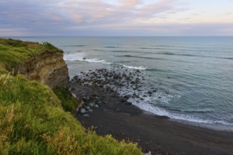 Seaside cliff with rocks and green vegetation under a cloudy sky, summer, Opunake, Taranaki, North