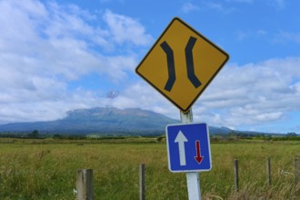 Road signs in front of a volcanic landscape Mount Taranaki under blue sky with clouds, summer,