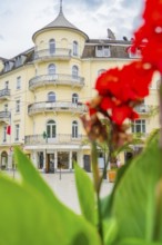 Yellow hotel with round balconies, emphasised by a red flower in the foreground, Baden Baden,