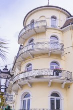 Historic hotel building in yellow with round balconies and surrounding lantern under a cloudy sky,
