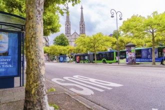 View of a street with trees and buses, a church with two towers rises in the background, Baden