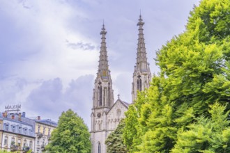 A gothic church with high towers in the background, surrounded by lush green foliage, Baden Baden,