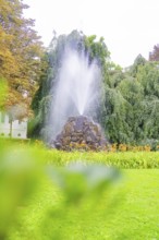 A tall fountain in a green park with lush vegetation and a relaxed atmosphere, Baden Baden, Germany