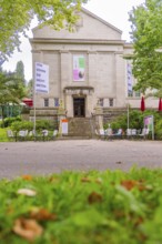 Historic building with signs and stairs, surrounded by trees and outdoor garden furniture, Baden
