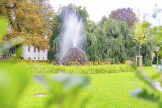 A bubbling fountain in a green park, surrounded by lush trees and flowers, creates a calm and