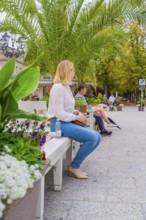 People sitting on a park bench surrounded by green plants and trees in the city, Baden Baden,