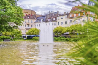 A fountain in an urban pond, surrounded by buildings and green vegetation, Baden Baden, Germany
