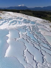 Terraces of turquoise water in white formations, mountains visible in the background under a clear
