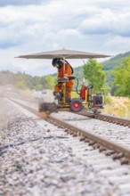 Worker on railway tracks uses a machine under a screen. Dust and nature in the background, grinding